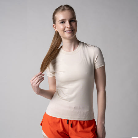 Gray background, image of a female model wearing a JOOLA women's club short sleeve, sandstone.