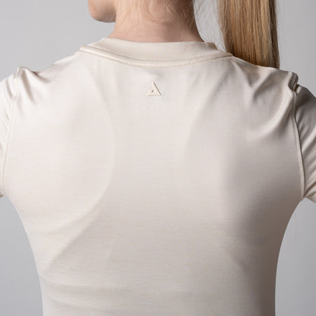 Gray background, image of the back of a female model wearing a JOOLA women's club short sleeve shirt, sandstone.