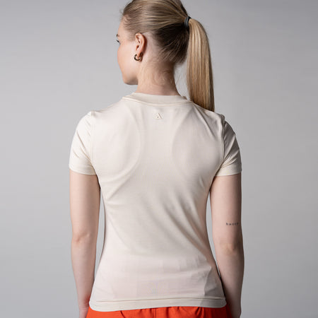Gray background, image of the back of a female model wearing a JOOLA women's club short sleeve, sandstone color.