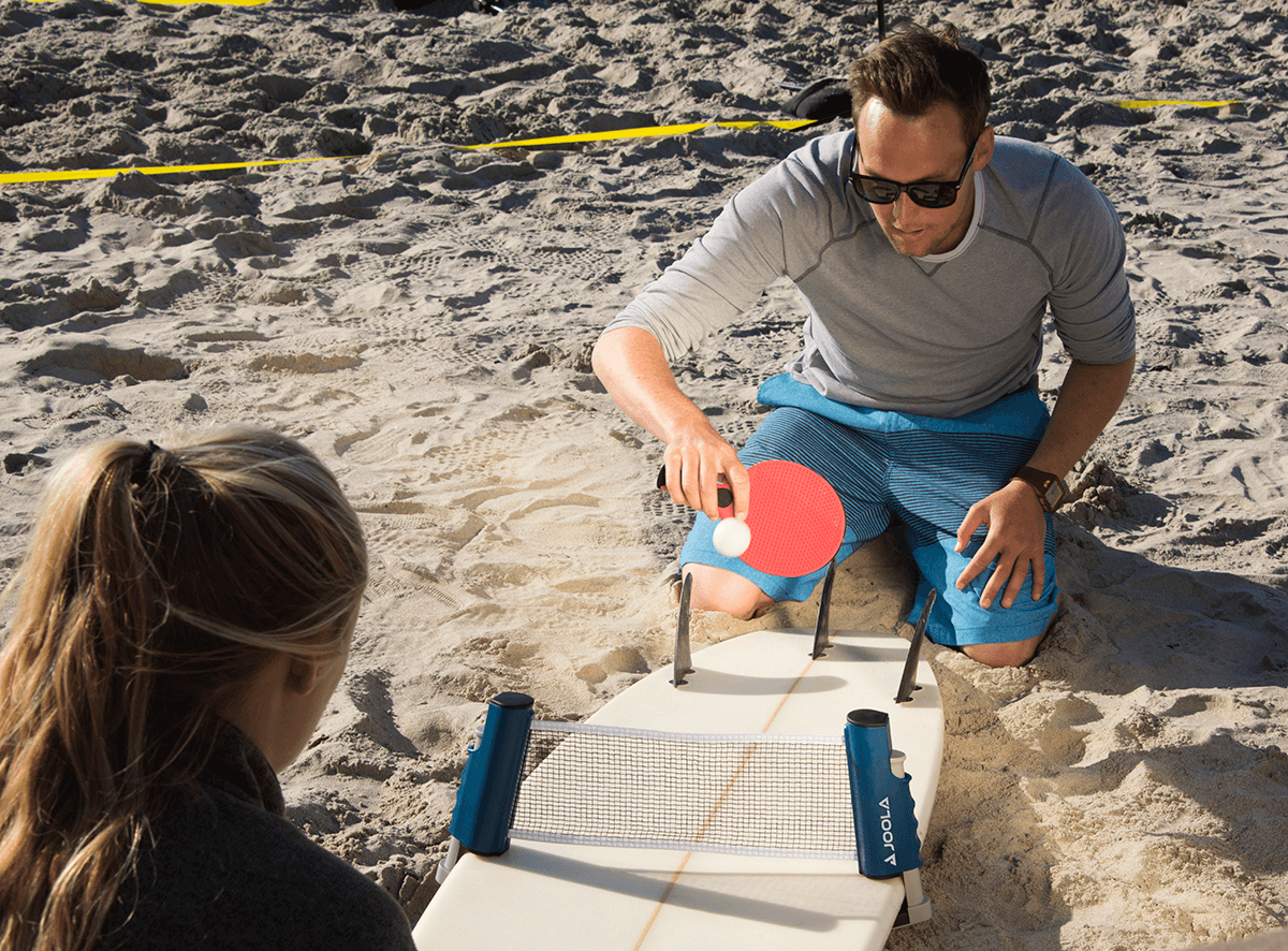 Image of two people playing table tennis on a surf board using the JOOLA retractable table tennis net.