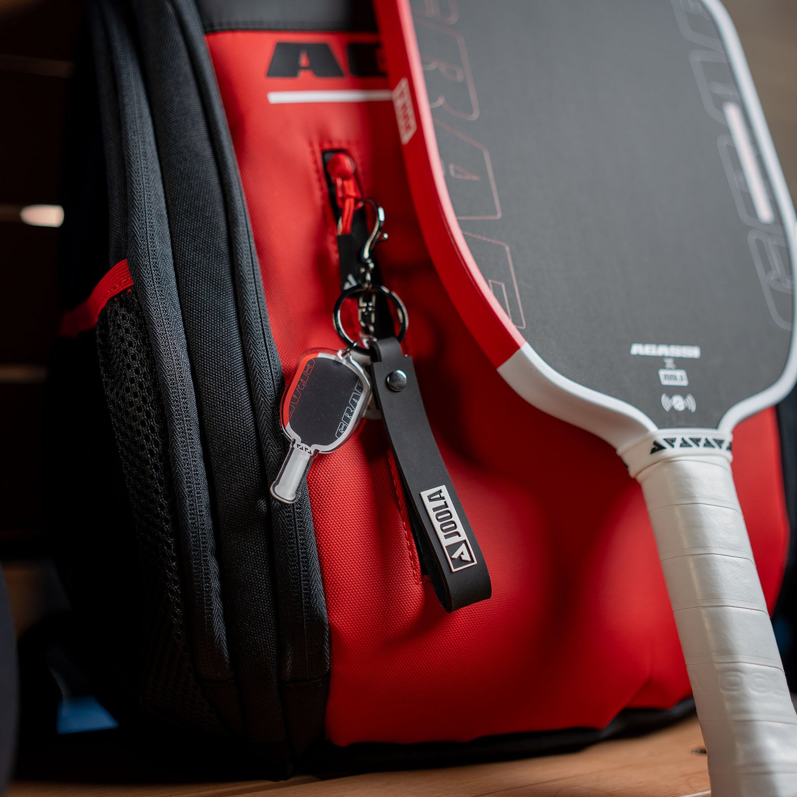 Agassi Vision red pickleball paddle bag with an Agassi Pro pickleball paddle and keychain on a wooden surface.