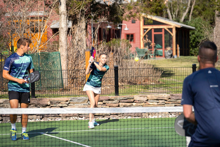 Action shot of Rachel Rettger and Ben Johns playing doubles with Eric White blurry in the foreground