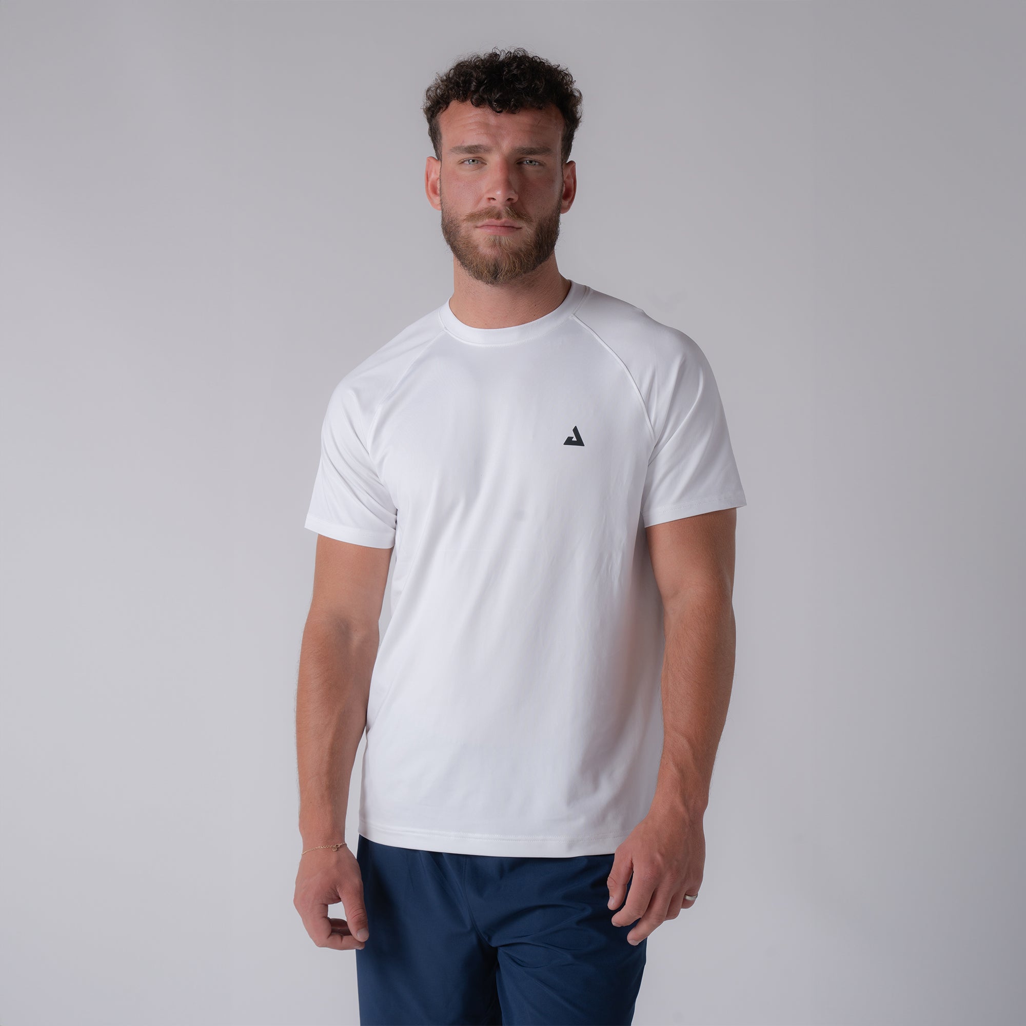 Image of a male model wearing a JOOLA men's court short sleeve shirt, white with black JOOLA trinity logo over the left chest.