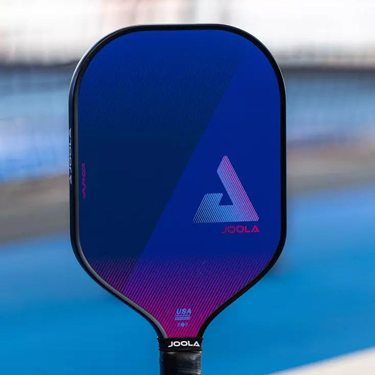 The JOOLA Wayfinder pickleball paddle with a blue-to-purple gradient face, standing upright on a blue pickleball court with a blurred background.