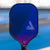The JOOLA Wayfinder pickleball paddle with a blue-to-purple gradient face, standing upright on a blue pickleball court with a blurred background.