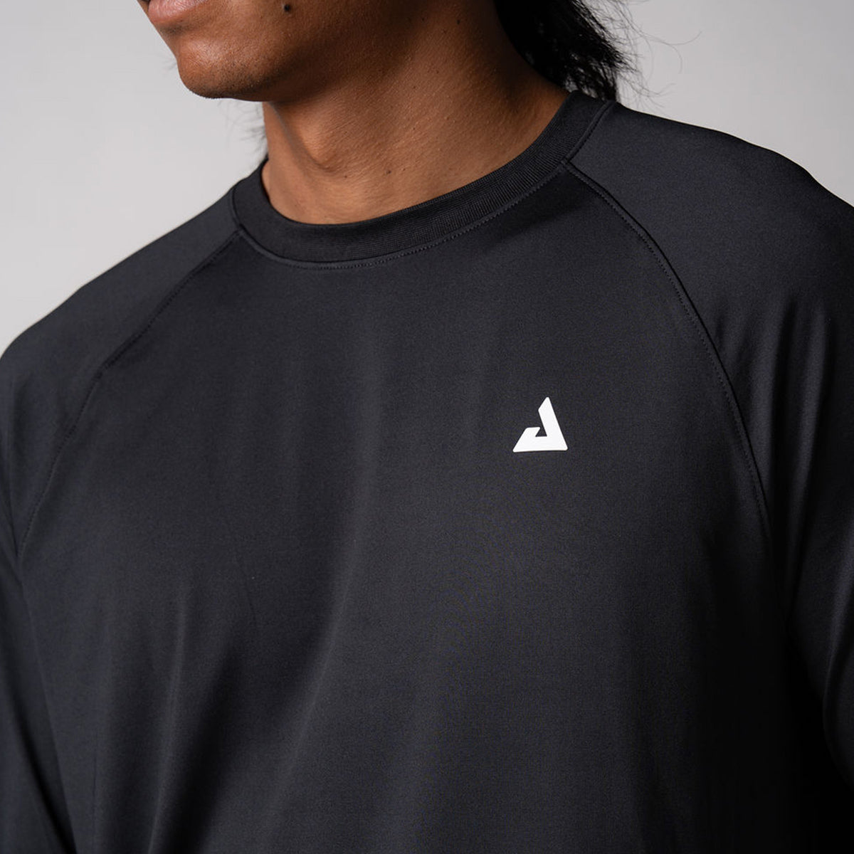 Close up image of the JOOLA Men's Long Sleeve Court shirt, black with a white trinity logo.