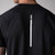 Close up image of the back of a JOOLA Men's Court Short Sleeve Shirt showing the JOOLA logo running down the center of the shirt, white logo on black shirt.