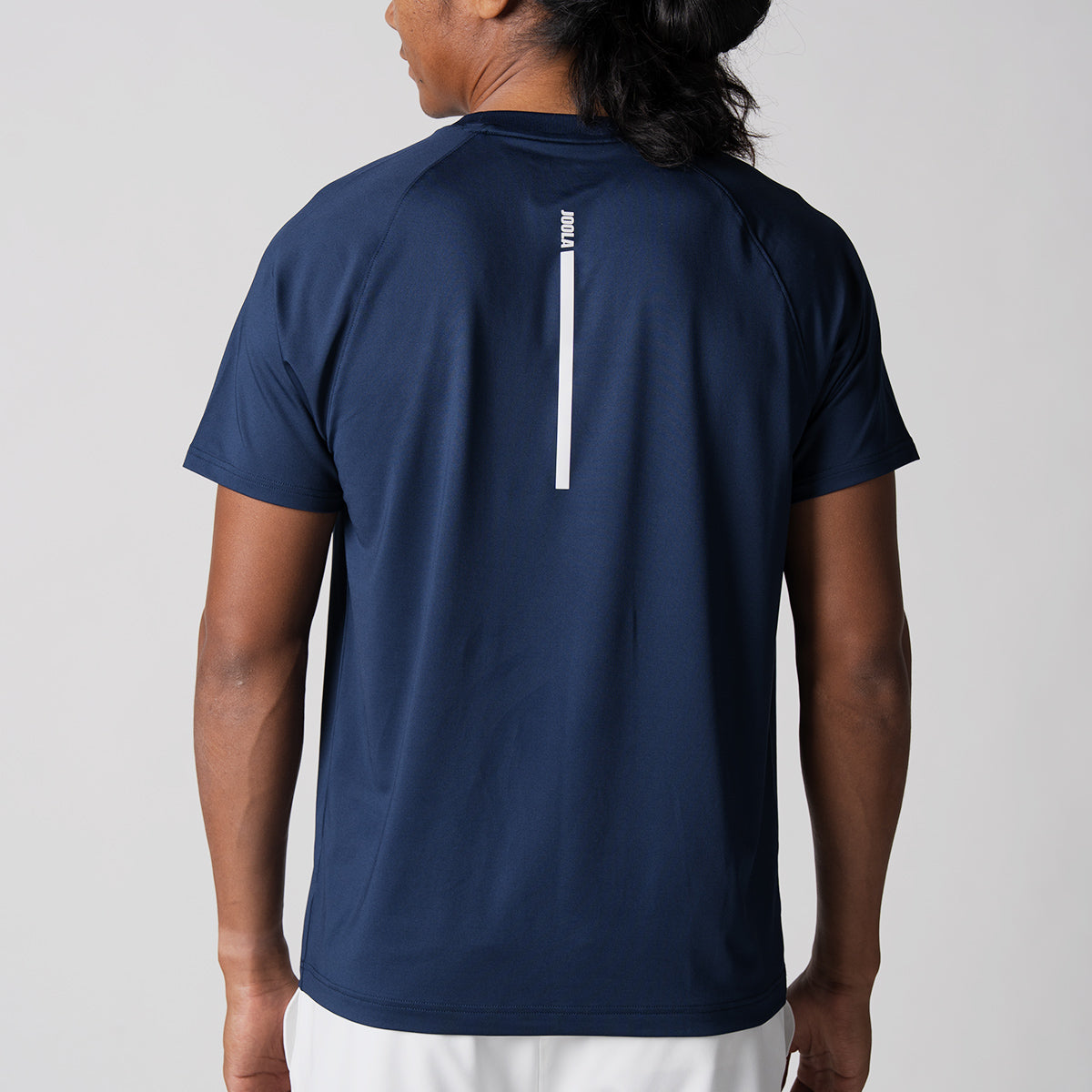 Image of a male model wearing a JOOLA Men's Court Short Sleeve shirt. The image shows the back of the shirt, navy shirt with white logo.