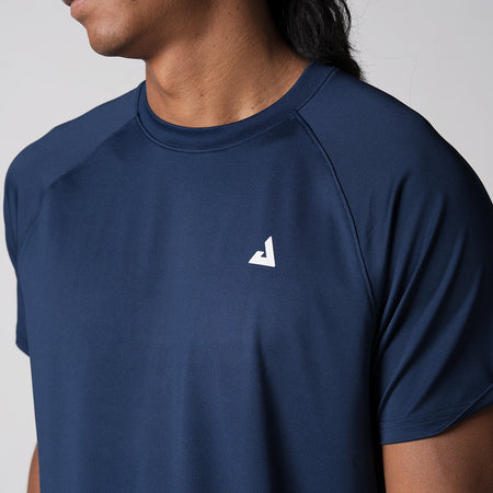 Close up image of the JOOLA trinity logo over the left side of the models chest who is wearing the JOOLA Men's Court Short Sleeve Shirt, Navy.