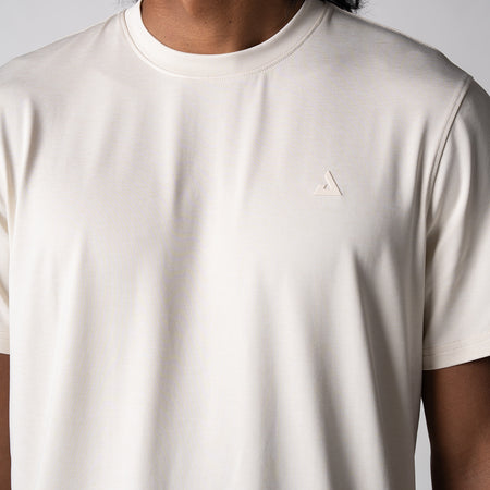 Gray background, close up image of the JOOLA trinity logo over the left chest on a male model who is wearing the JOOLA men's club short sleeve, sandstone color.