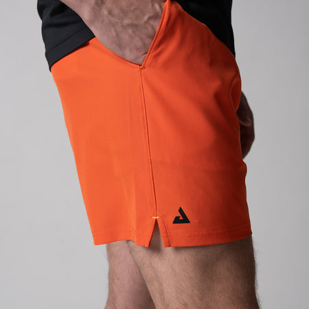 Gray background, close up of a black JOOLA trinity logo on the right leg of a pair of Men's Woven Short, poppy red.