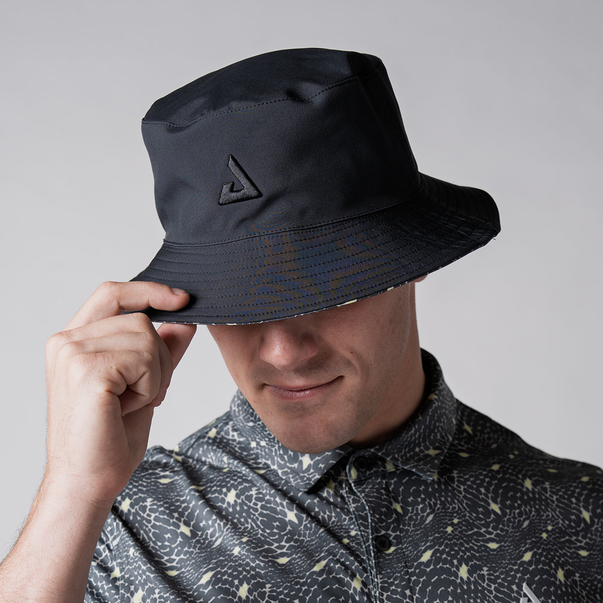 Close up image of a male model wearing a reversible bucket hat. Black.