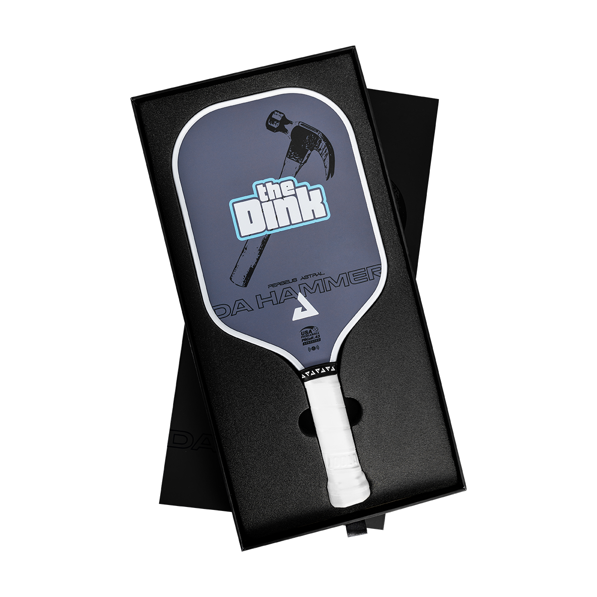 A pickleball paddle presented in an open black gift box on a white background. The paddle has a dark slate-blue face with a hammer graphic, the text 'the Dink', and 'DA HAMMER', plus a white grip.