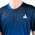 White background, close up on the white JOOLA Trinity Logo on a JOOLA Men's Competition Table Tennis shirt.