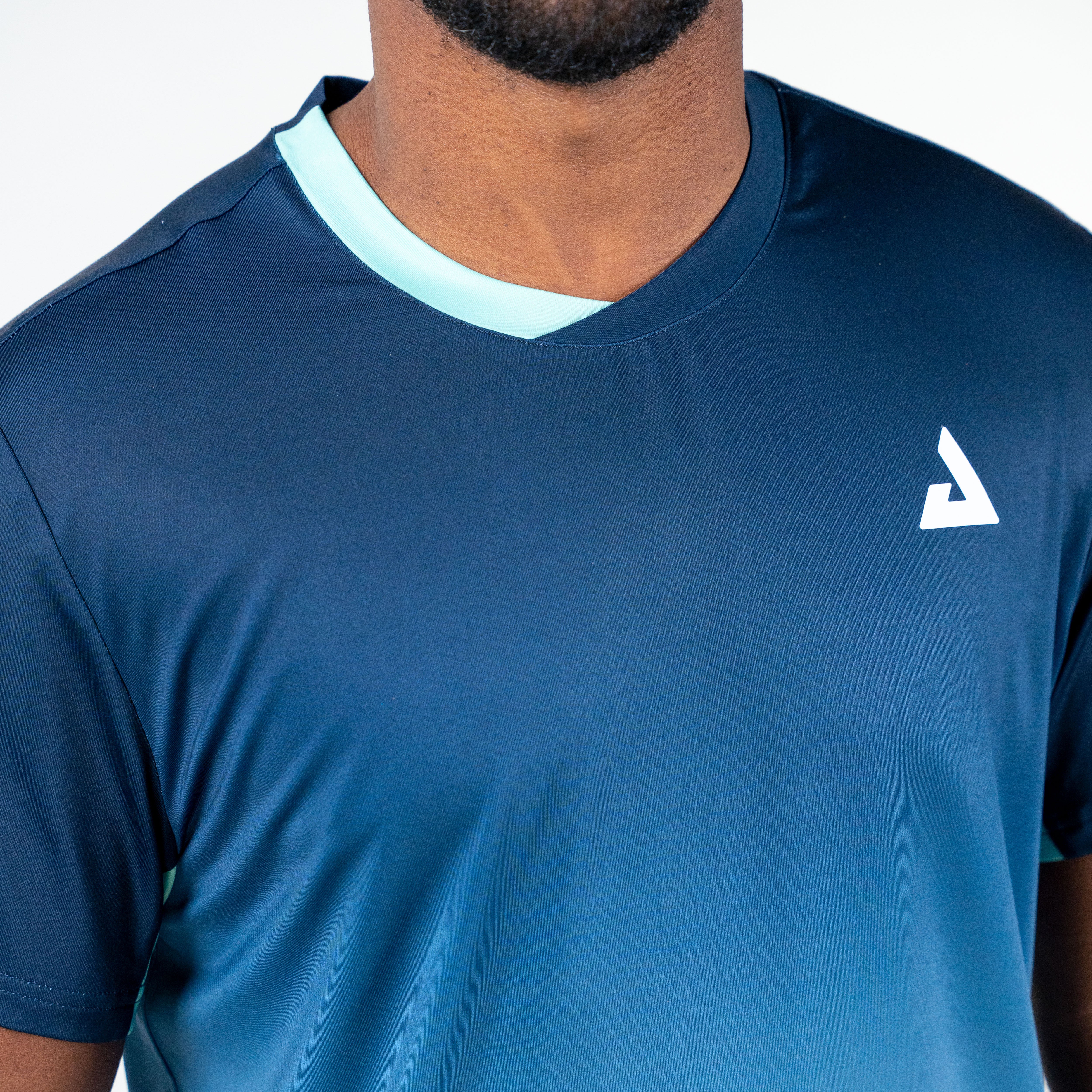 White background, product image showing a close up on the JOOLA Men's Competition table tennis shirt, half turqoisue and half blue.