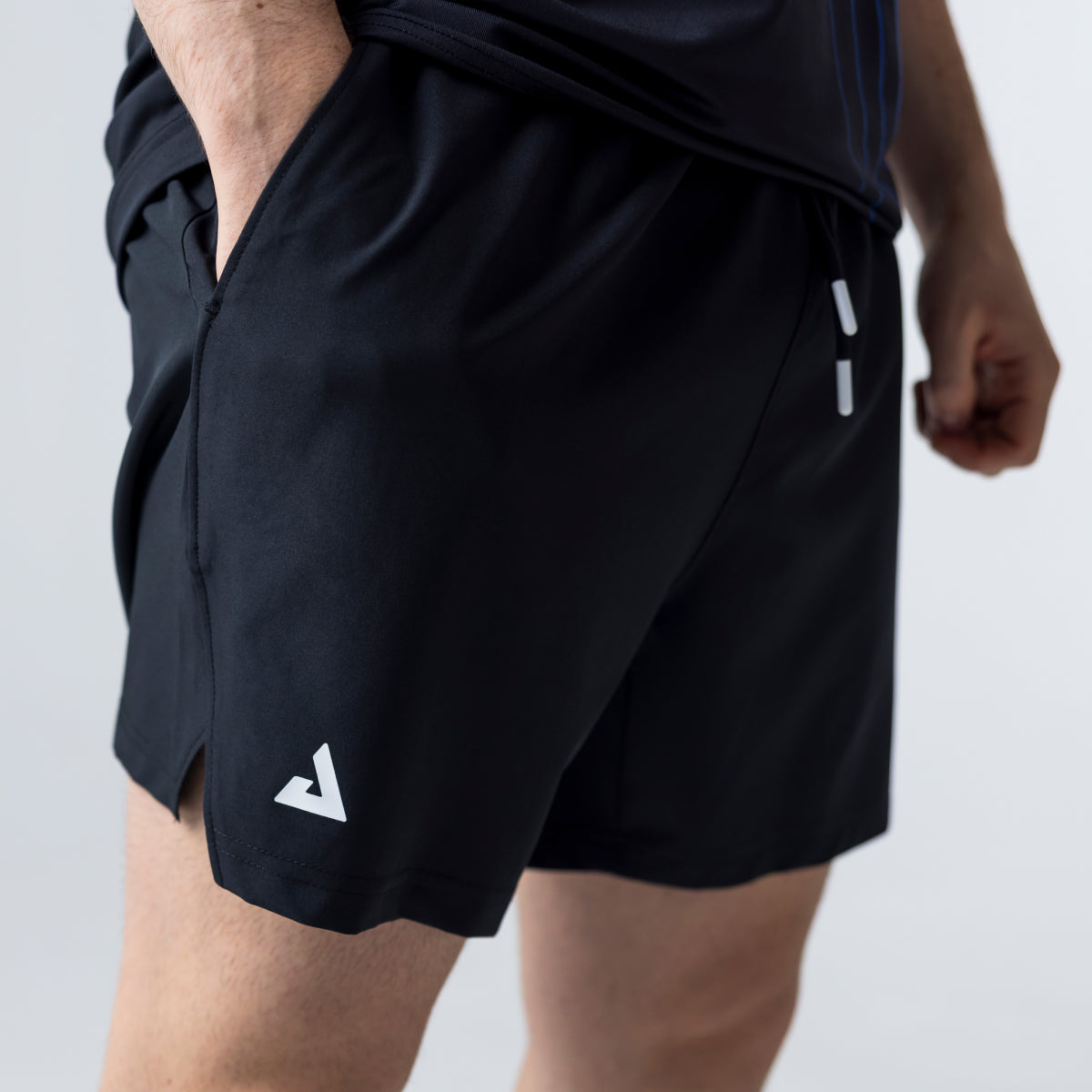Gray background, close up images of a pair of JOOLA Shorts, black with white trinity logo.