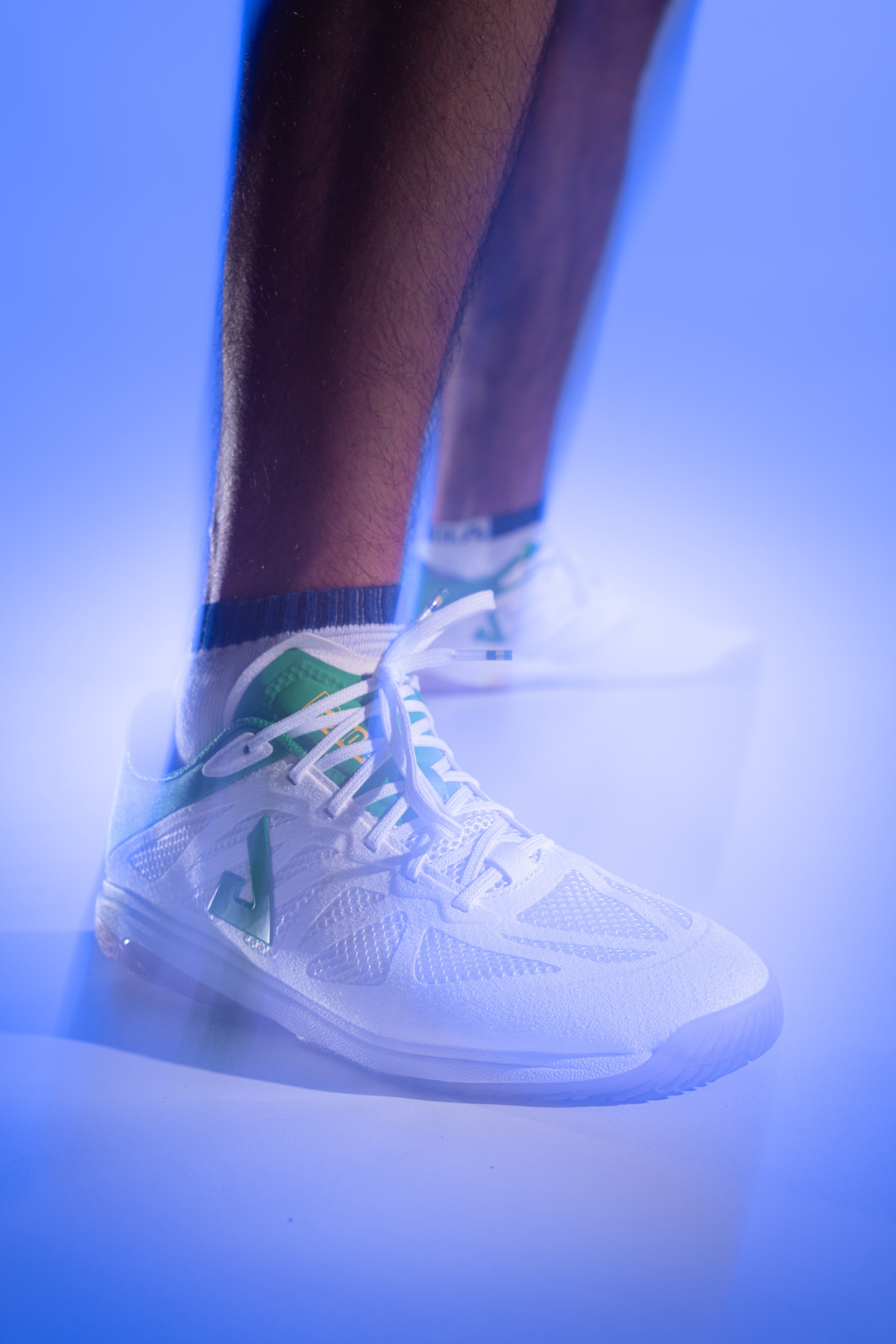 Purple gradient background, product image showing a models wearing a pair of white and green JOOLA TT SM4SH table tennis shoes.