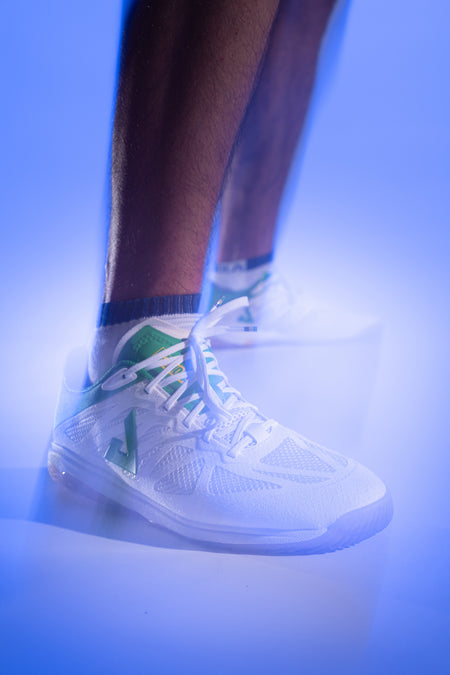 Purple gradient background, product image showing a models wearing a pair of white and green JOOLA TT SM4SH table tennis shoes.