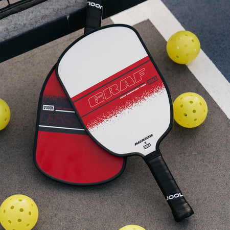 Close up image of the Graf and Agassi pickleball paddles laying on the pickleball court with pickleballs around them.