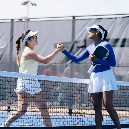 Two women shaking hands across a pickleball net on a court.