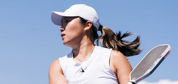 Woman holding a pickleball paddle against a clear blue sky.