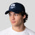 Person wearing a navy blue JOOLA Collegiate Cotton cap with a logo on a light gray background