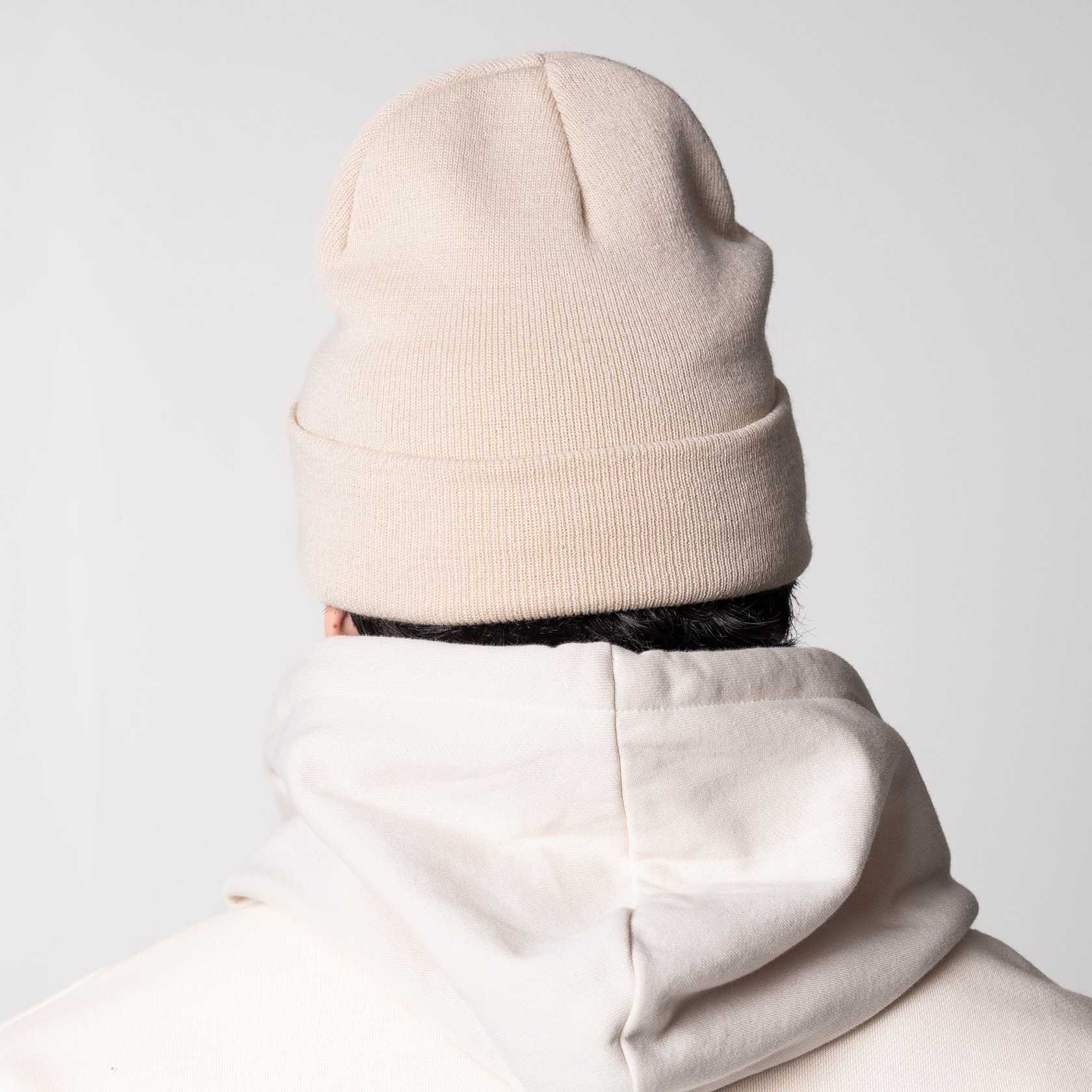 Person wearing a sandstone colored JOOLA cuff beanie and light-colored hoodie against a plain background