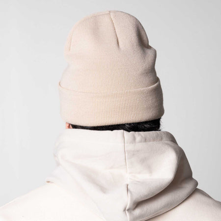 Person wearing a sandstone colored JOOLA cuff beanie and light-colored hoodie against a plain background