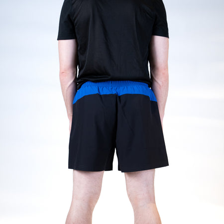 White background, product image showing the rear view of a male model wearing a pair of black and blue JOOLA x Hugo Calderano shorts.