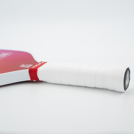 A close-up of a JOOLA pickleball paddle handle wrapped in white grip tape with a red band, showing part of the red and white blade against a clean white background.