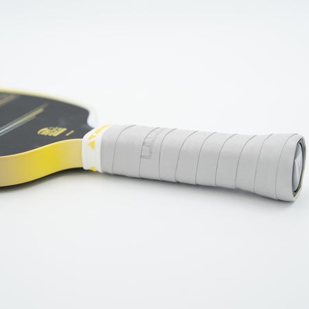 A close-up of a pickleball paddle handle wrapped in light gray JOOLA Overgrip with part of the paddle face visible in yellow and black on a clean white background.