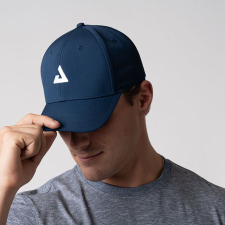 Male model wearing a JOOLA Essential Cap, pointing the hat down so you can see the JOOLA trinity logo on the front of the hat, Navy.