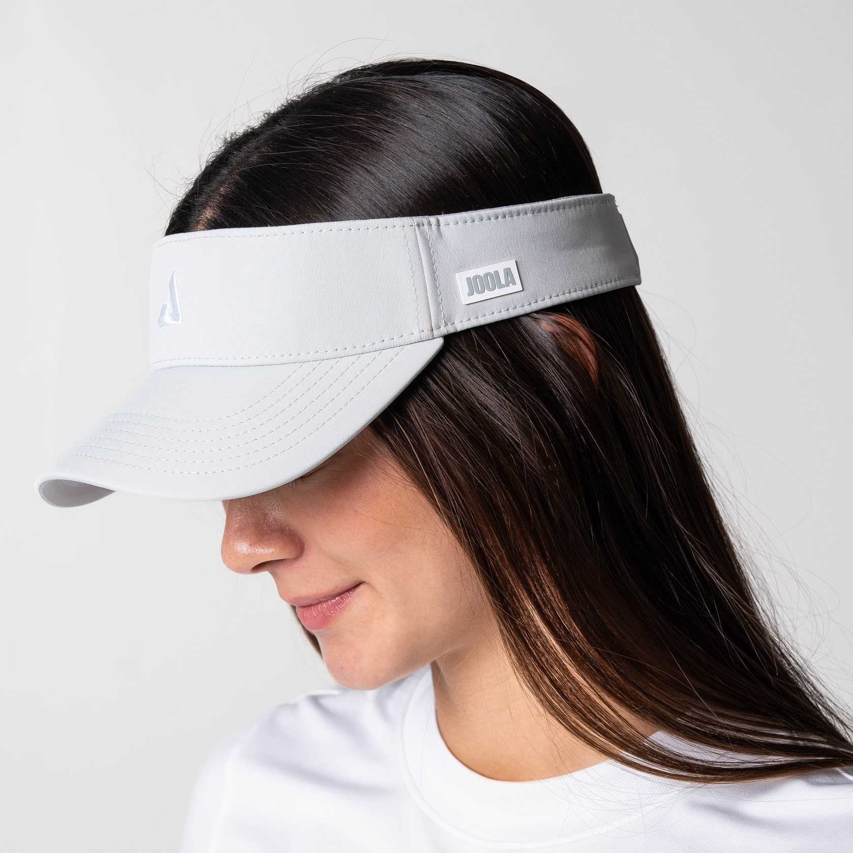Gray background, image of a female model wearing a JOOLA Essential Visor, Gravity Gray.