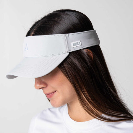 Gray background, image of a female model wearing a JOOLA Essential Visor, Gravity Gray.