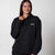 Gray background, image of a female model wearing a JOOLA Fleece Hoodie, Black.