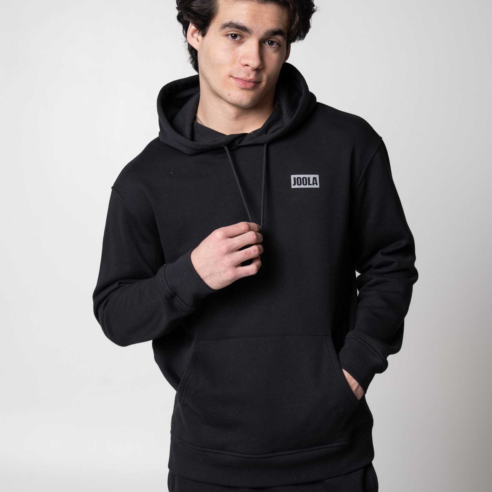 Gray background, image of a male model wearing a black JOOLA Fleece Hoodie.