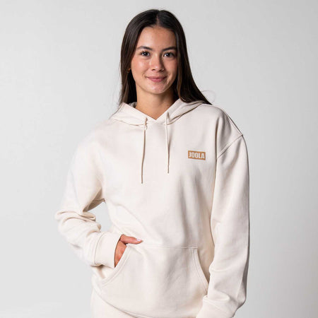 Gray backround, image of a female model wearing a sandstone colored JOOLA fleece hoodie.