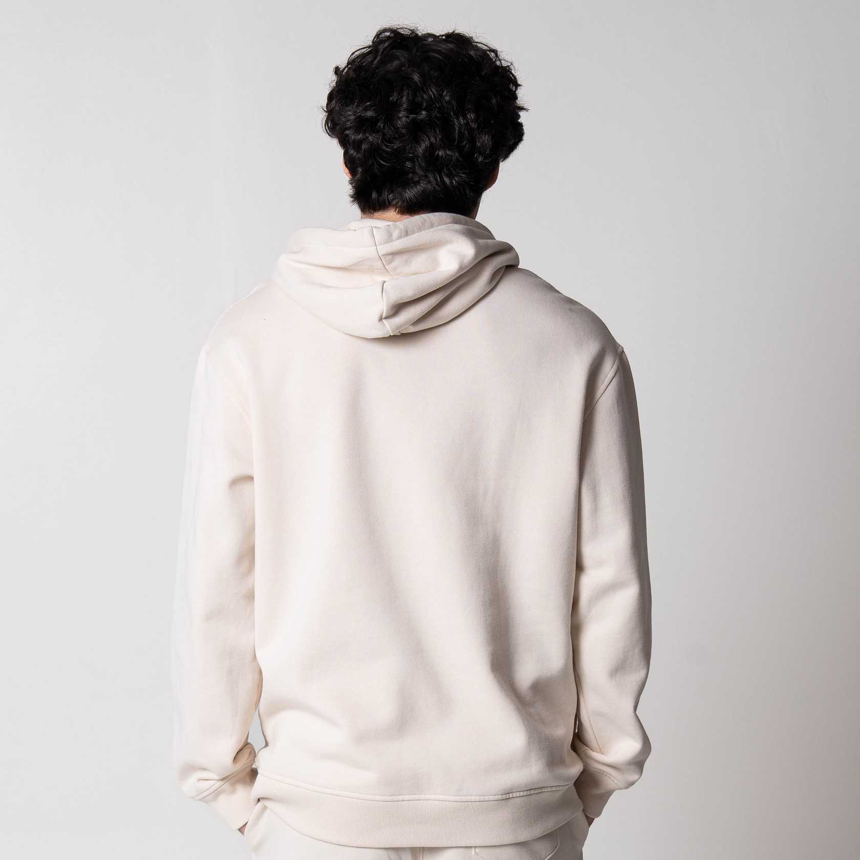 Gray background, image showing the back of a male model who is wearing a JOOLA Fleece Hoodie, Sandstone colored.