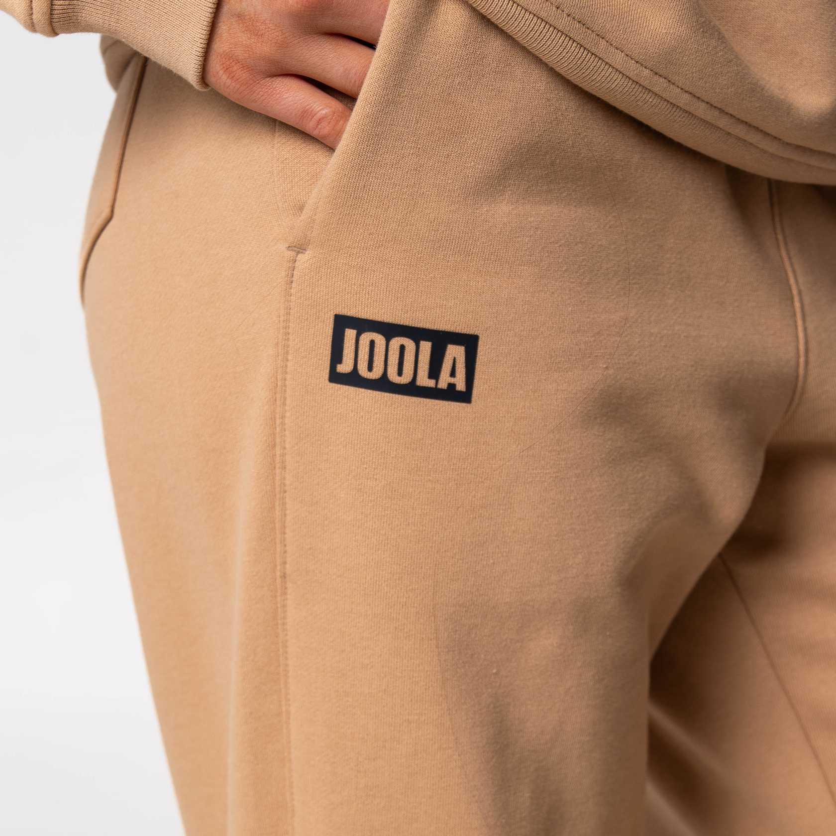 Close up on the JOOLA logo on a pair of JOOLA Fleece Pants, Latte.