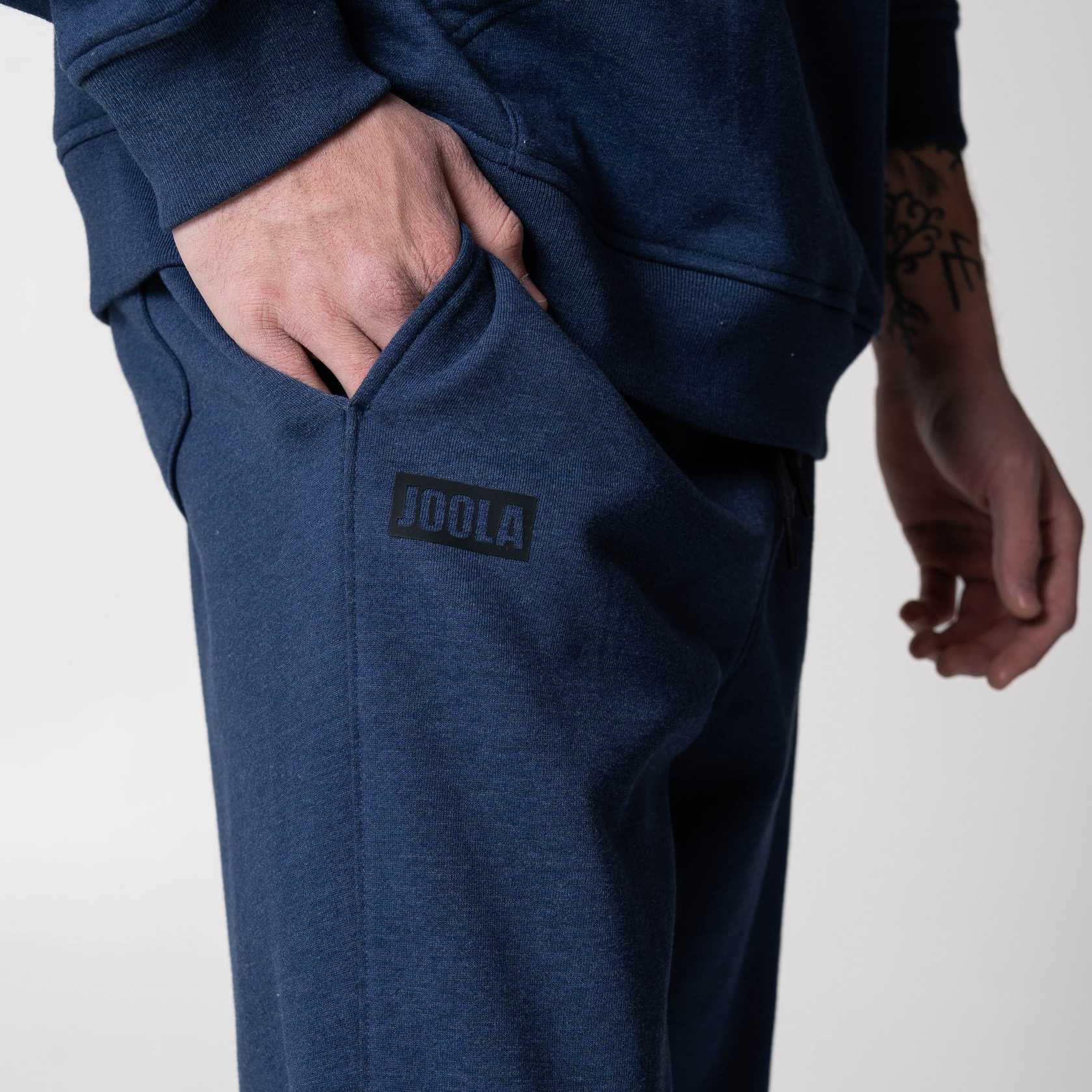 Gray background, close up on the black JOOLA logo on a pair of JOOLA Fleece Pants, Navy.