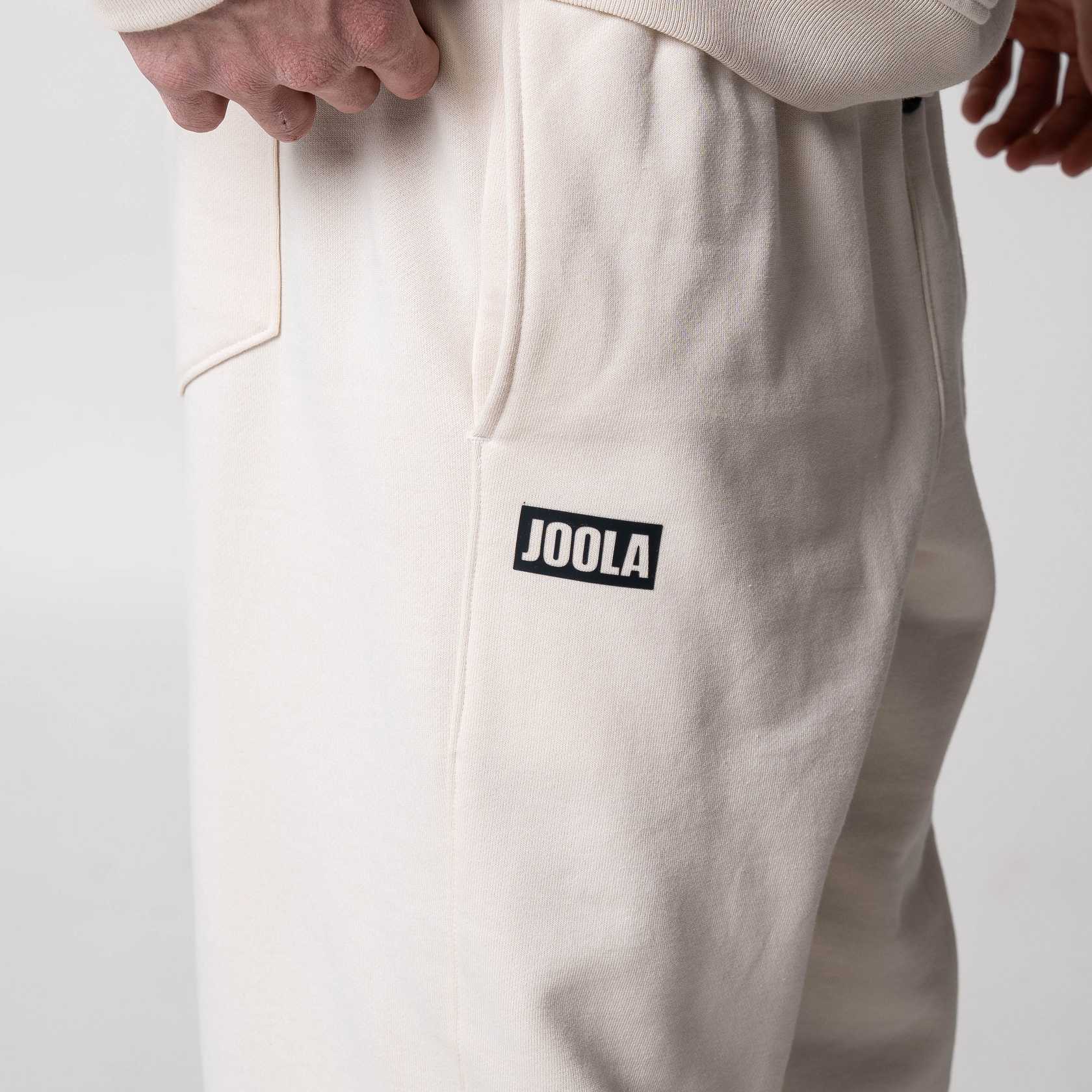 Gray background, close up of the JOOLA logo on the side of a air of fleece pants.