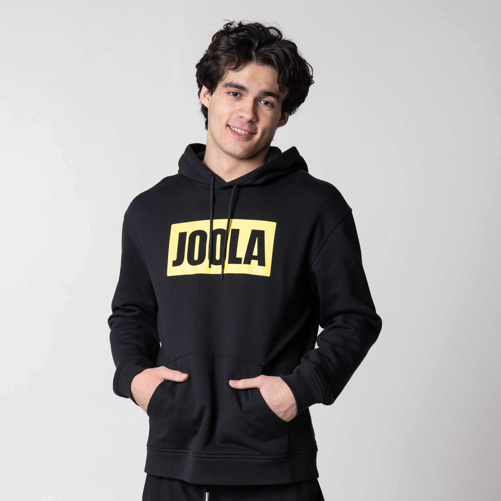 Gray background, image of a male model wearing a black JOOLA Graphic hoodie.