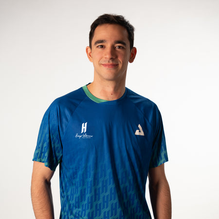 White background, image of JOOLA pro Hugo Calderano wearing a Hugo Calderano monogram crossover raglan short sleeve shirt.