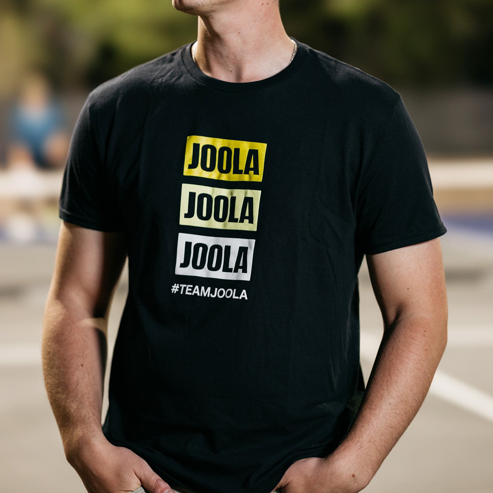 Close up image of a male model wearing a black JOOLA Staked Logo Graphic Tee.