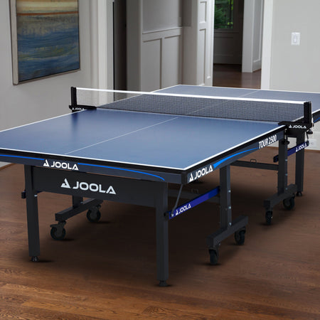 JOOLA table tennis table in a room with wooden flooring and a painting on the wall.