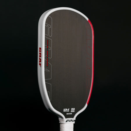 Black background, slightly angled product image of the Agassi x JOOLA Graf Pro pickleball paddle with white handle, black surface and white and red edge guard.