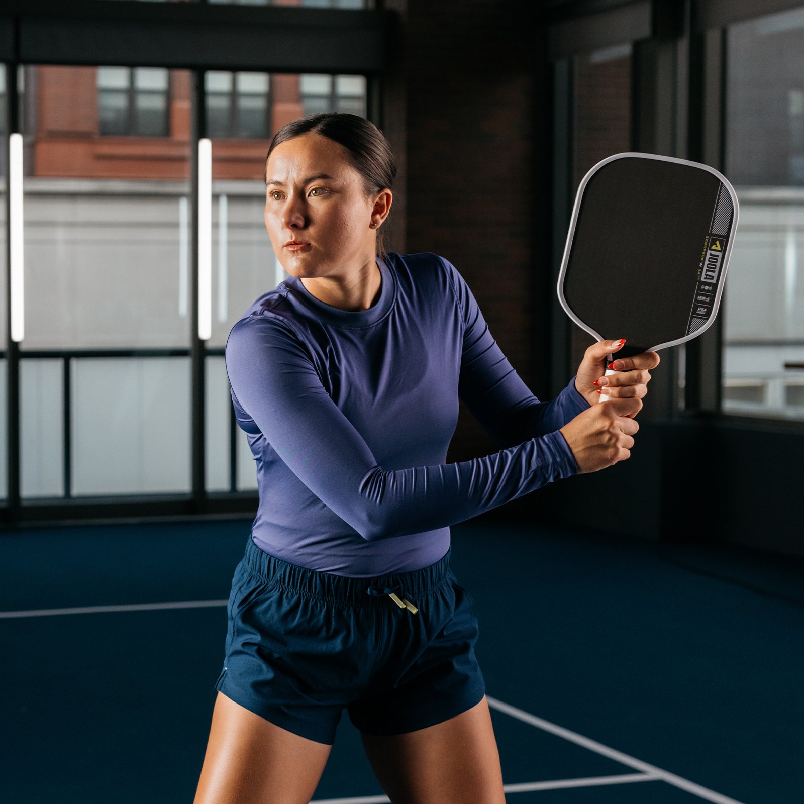 Image of JOOLA Pro Anna Bright with her JOOLA Pro IV Scorpeus signature paddle in her hands on an indoor pickleball court.