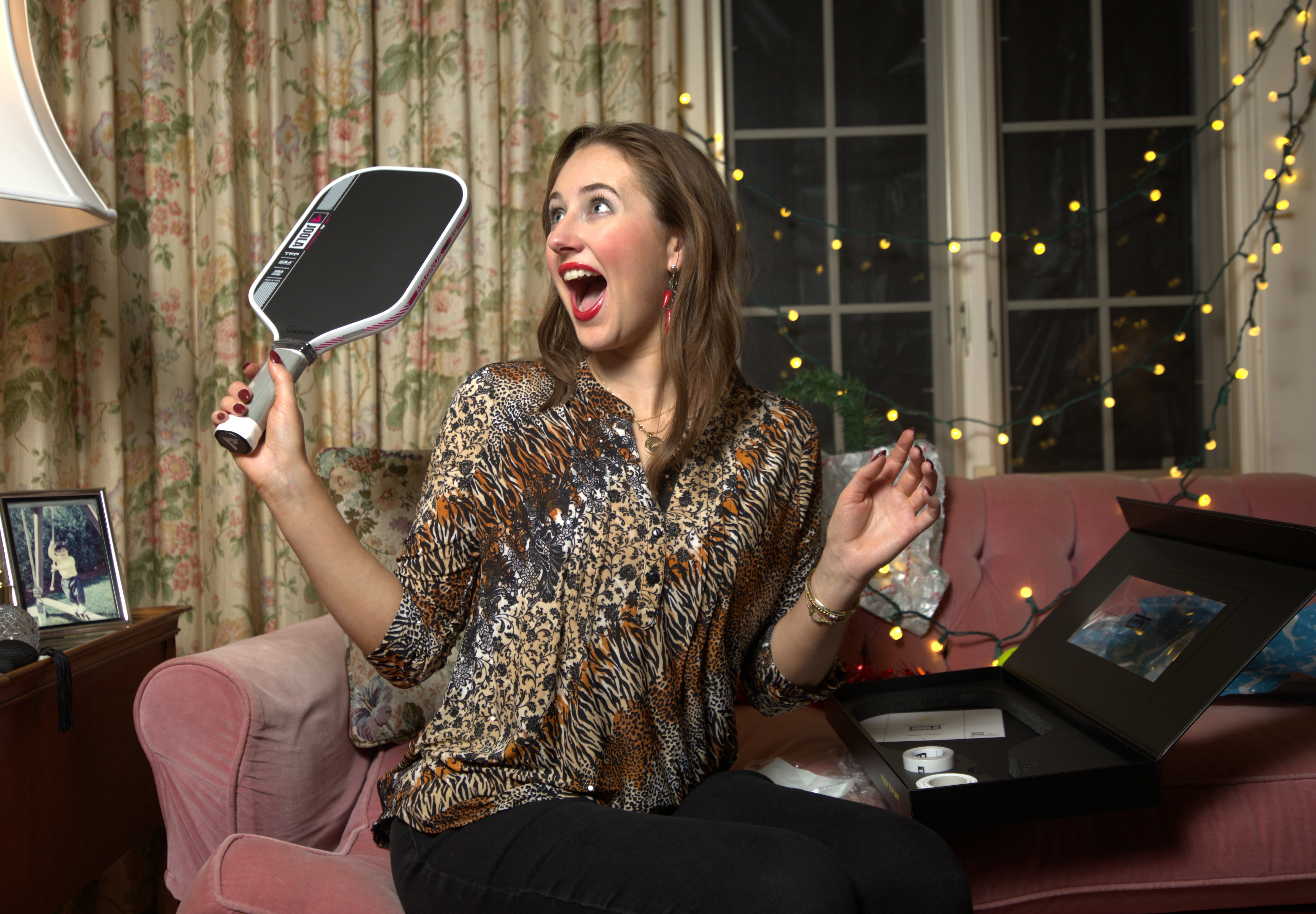 Woman holding a pickleball paddle in a living room with festive lights.