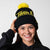 Gray background, image of a model wearing a black and yellow JOOLA Pom Pom Beanie.