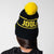 Gray background, image of a model wearing a black and yellow JOOLA Pom Pom Beanie.